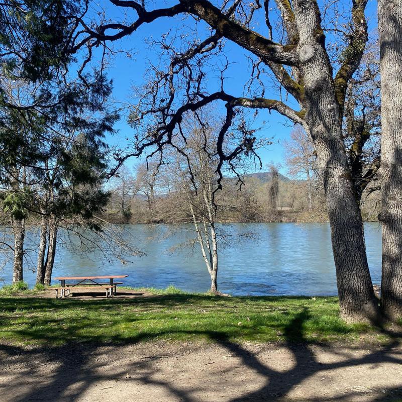 Picnic table by a river with trees and hills in the background.